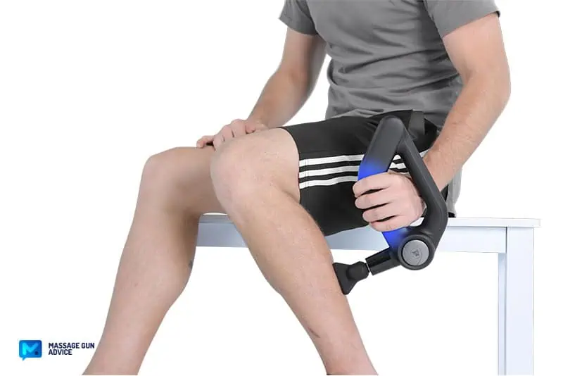 a man holding a massage gun with the left hand while treating the his left calf.
